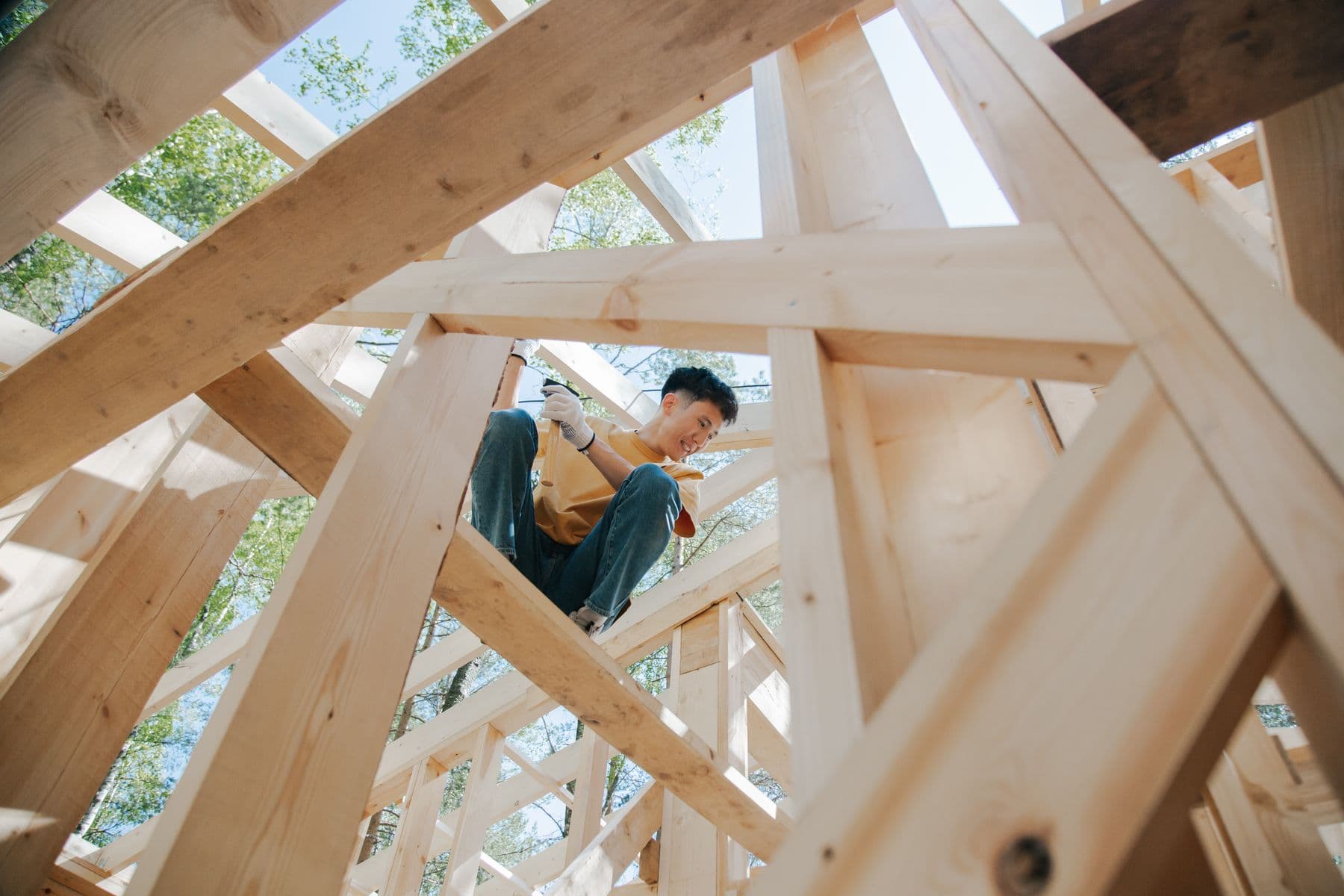 A carpenter fastening framing lumber inside the timber skeleton of a house under construction.